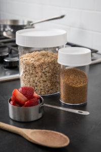Oats and brown sugar are stored in 8oz Storage Jars, with sliced strawberries in a measuring cup and a wooden spoon beside them.