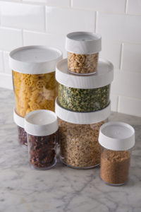 Seven clear 8oz Storage Jars with white lids, filled with pasta, beans, oats, and grains, sit neatly on a marble countertop.