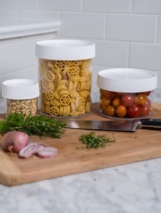 Three 4oz Storage Jars filled with pasta, cherry tomatoes, and pine nuts sit on a cutting board with herbs, shallot, and a knife.