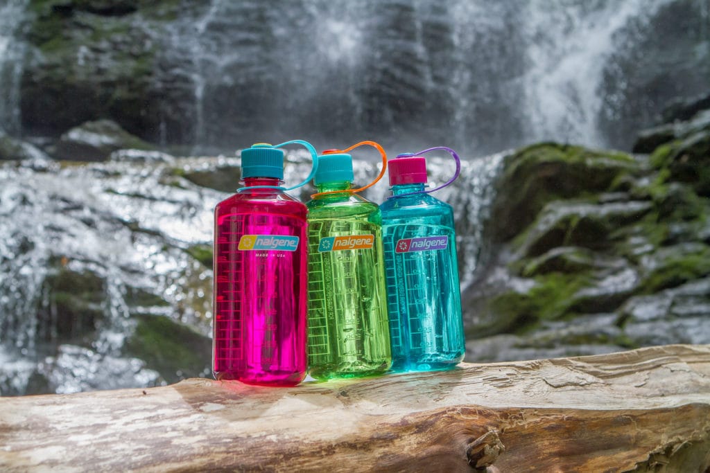 Three colorful Nalgene water bottles sit on a log in front of a waterfall and rocks.
