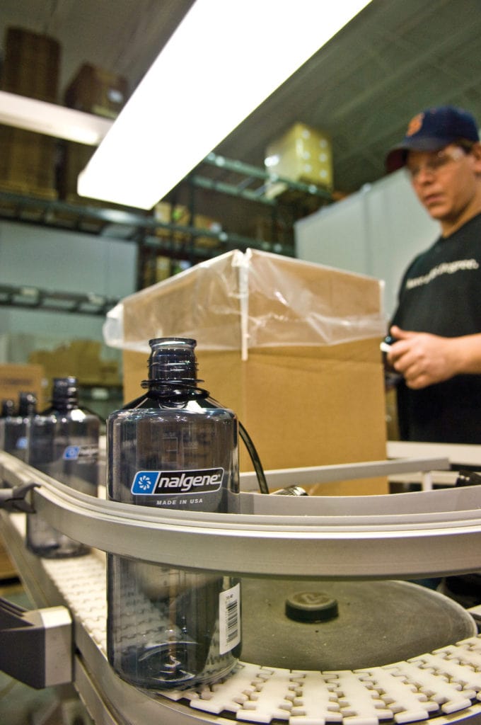 A Nalgene bottle on a conveyor belt with a worker and boxes in the background.