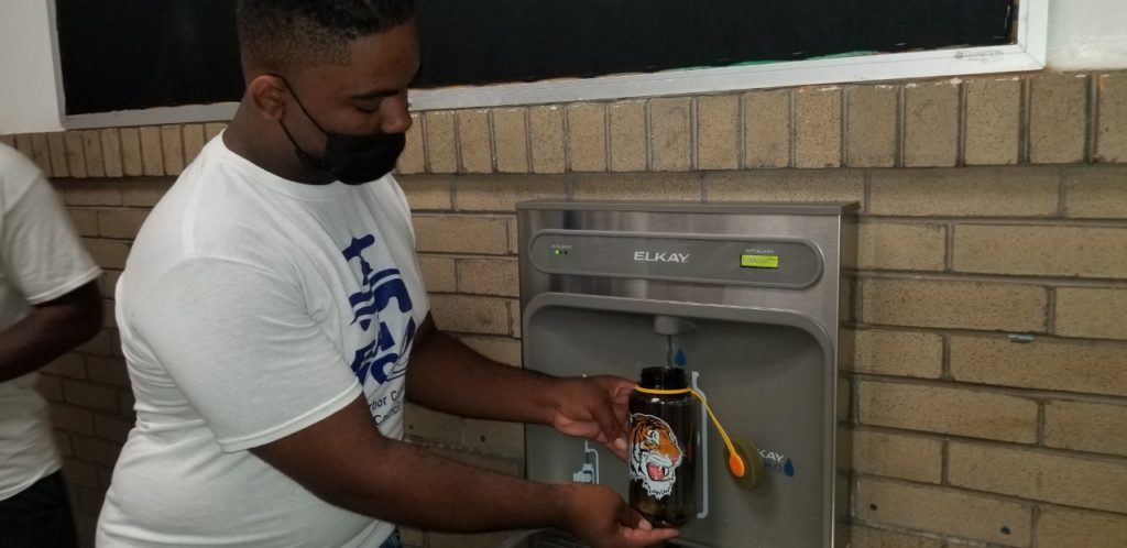 A man in a mask fills a tiger-decorated bottle at a water filling station.