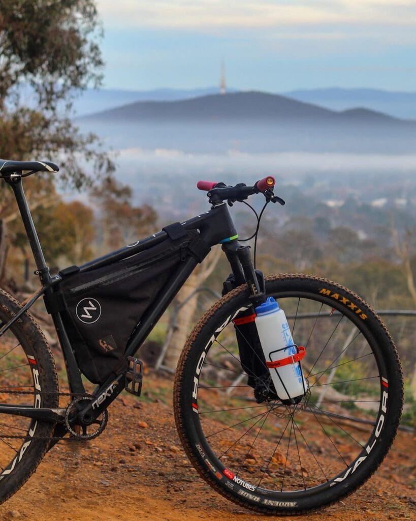 A mountain bike on a dirt trail overlooks a misty valley with hills and a distant tower in the background.