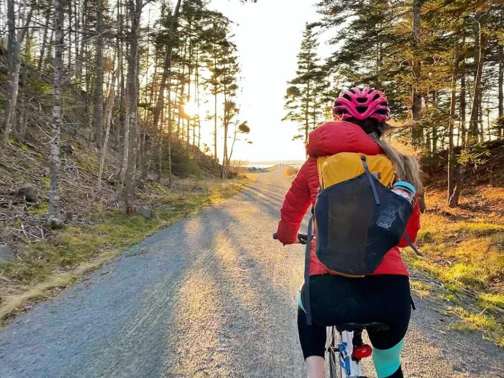 A cyclist with a red helmet rides on a forest trail at sunset.