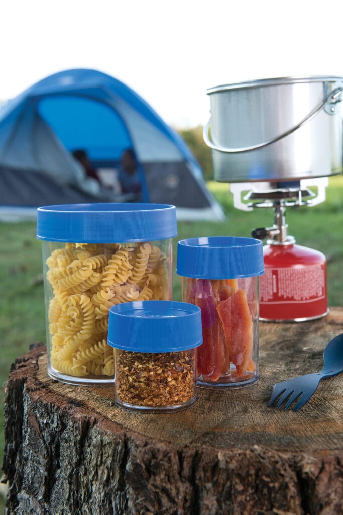 Three 32oz Storage Jars - Blue Lid hold pasta, dried food, and spices on a tree stump at a campsite next to a tent.