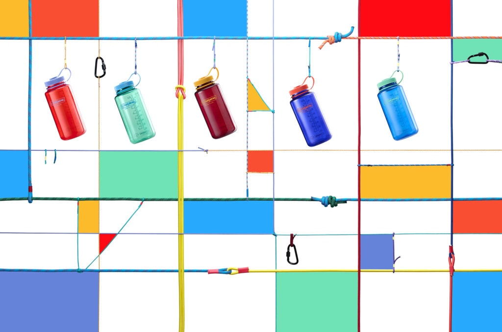 Six colorful water bottles hang from ropes against a bright, geometric, multicolored background.