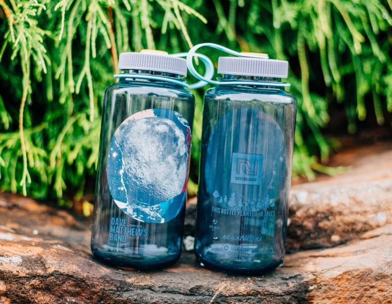 Two reusable water bottles with nature designs placed on a rock with green foliage in the background.