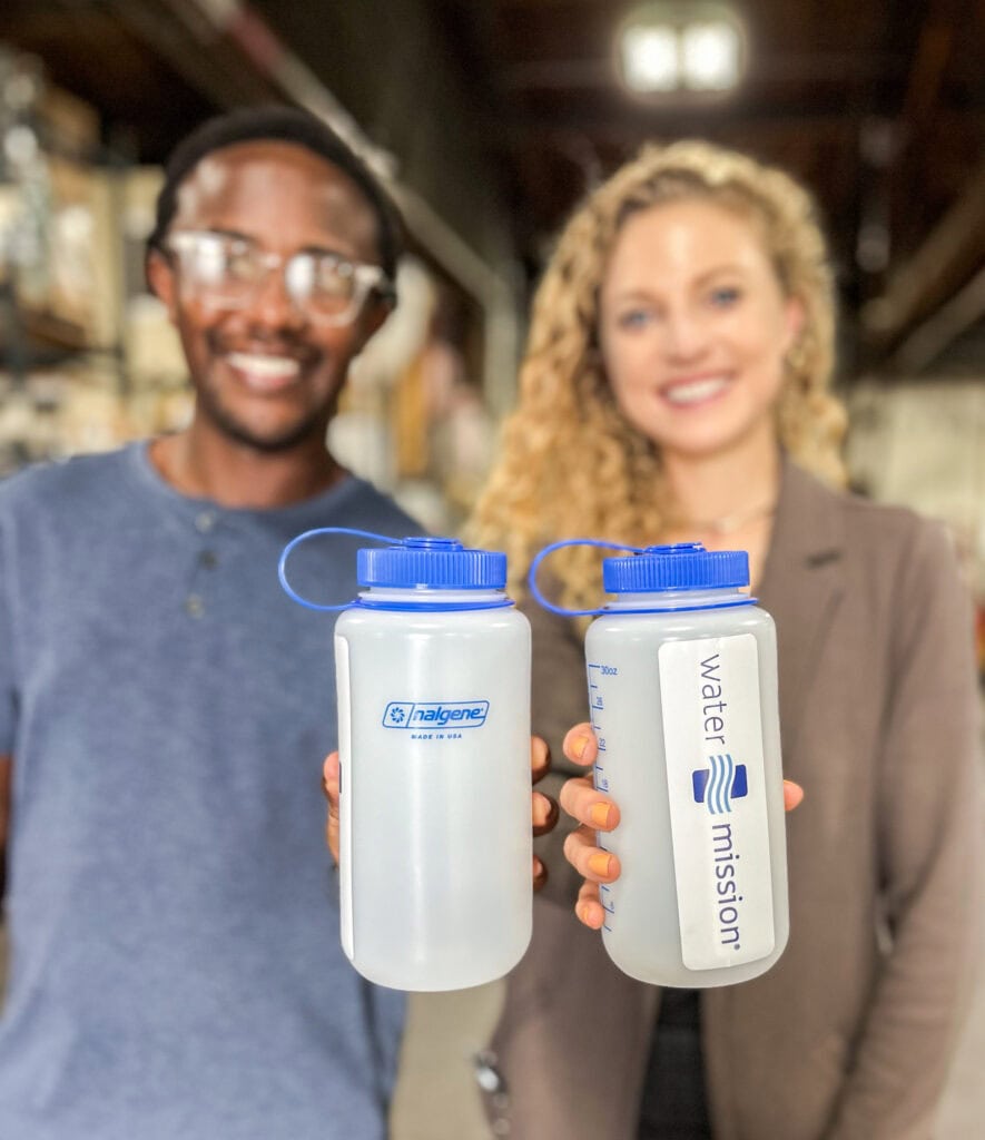 Two people smiling and holding clear water bottles with blue lids, one labeled "Nalgene" and one "Water Mission".