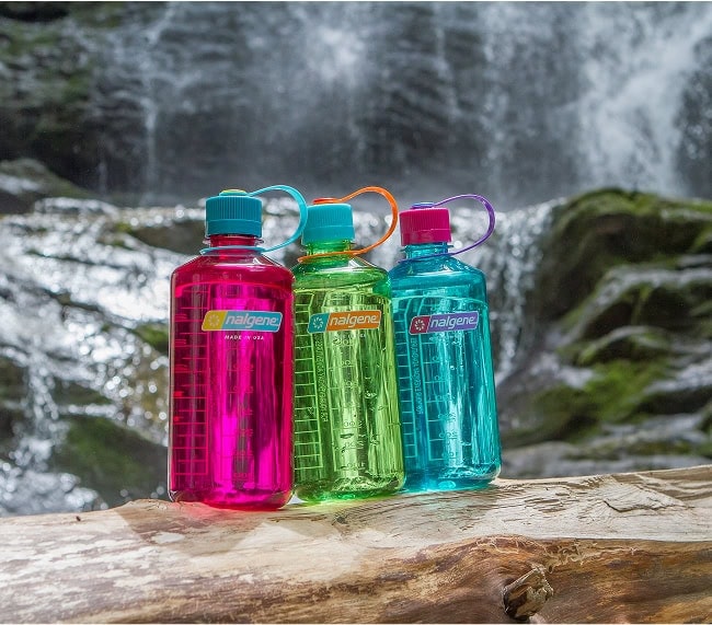 Three colorful water bottles sitting on a log near a waterfall.