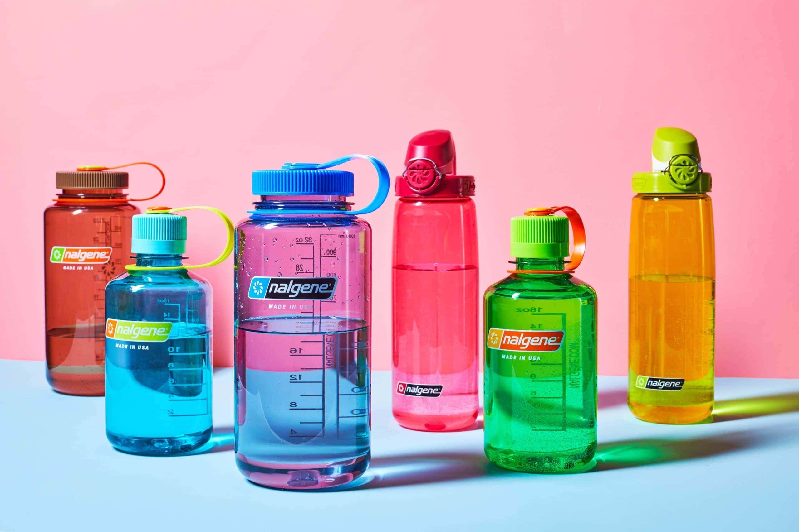 Six colorful Nalgene water bottles are arranged on a pink and blue background.